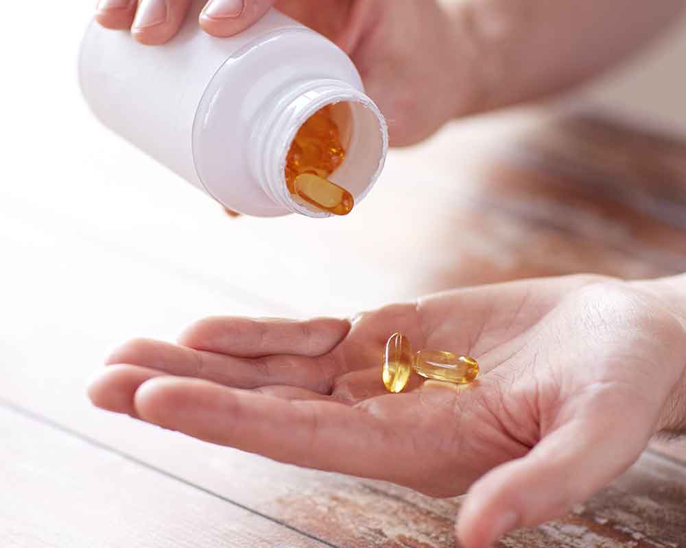 Woman hand pouring soft gel pills out of white plastic bottle
